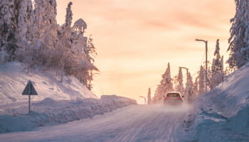 A car travels along a snow-covered road lined with frosted trees.