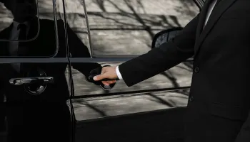 A man in a dark suit holds the door handle of a black van.